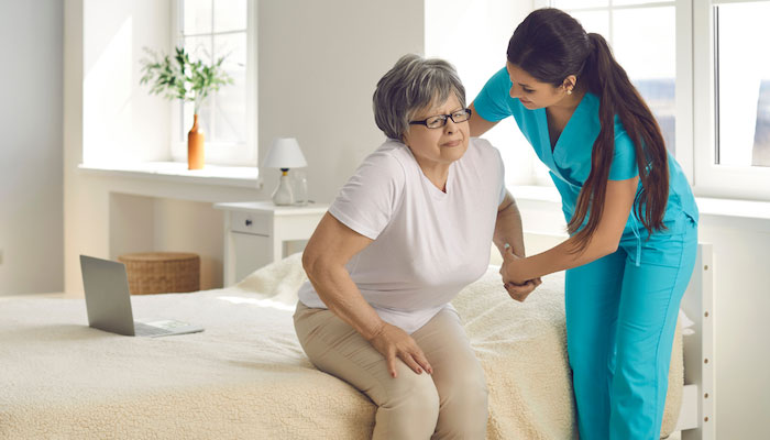 Caregiver helps older woman off bed