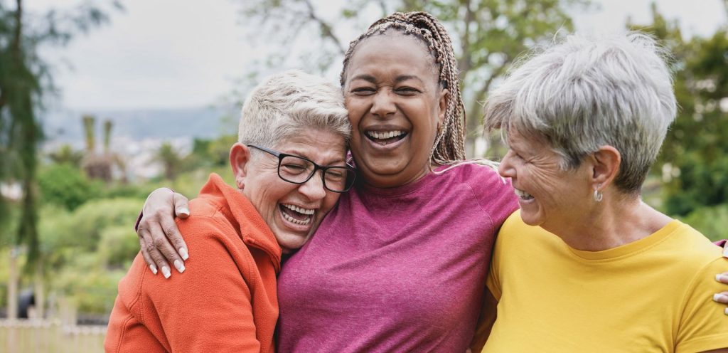 Three older adult woman hug and laugh together