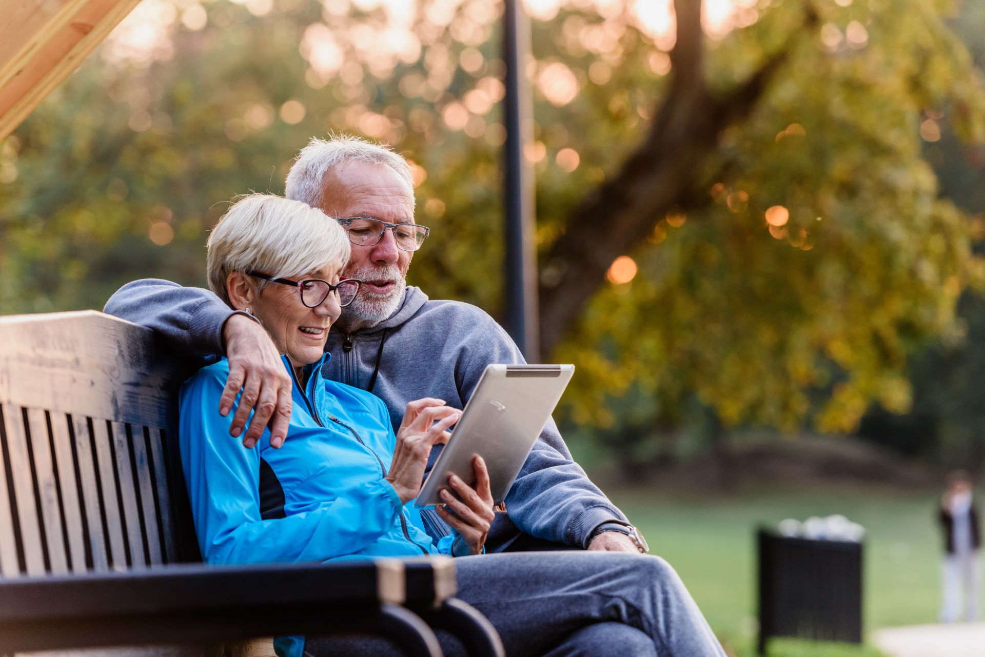 An older couple sits together reading on a park bench outdoors