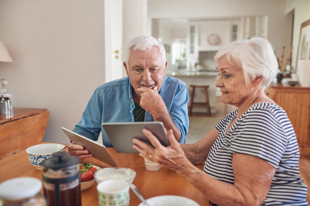Older adult couple looking at Medicaid versus Medicare on tablets.