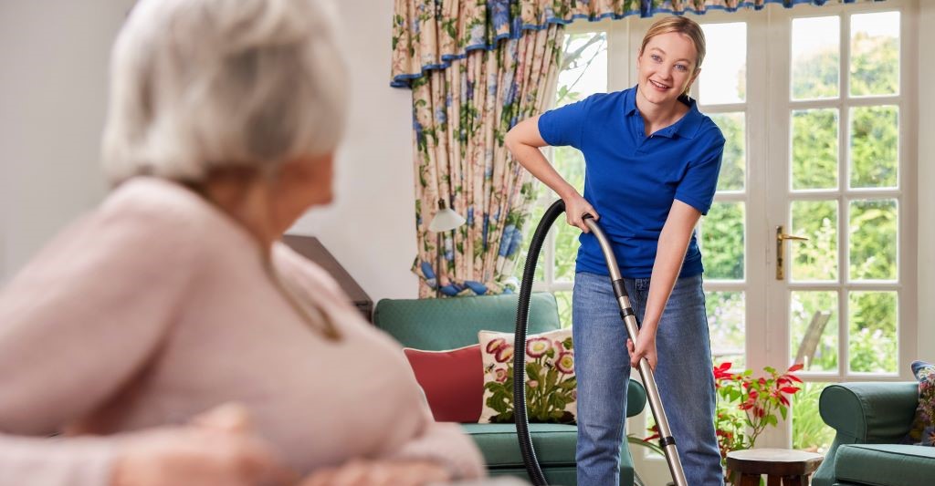 Older adult woman watches her caregiver clean the house