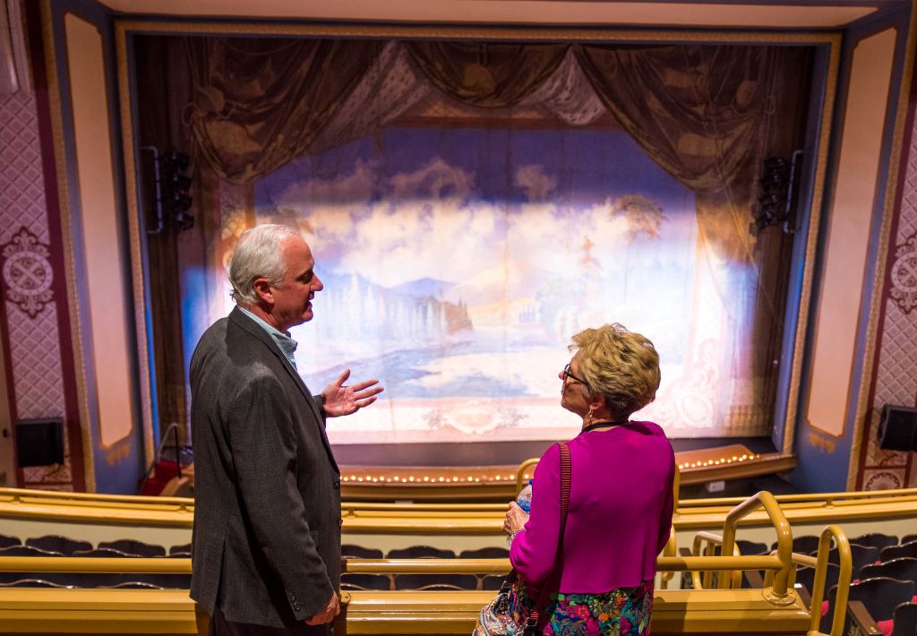 Two adults stand in a theater's mezzanine looking at the stage