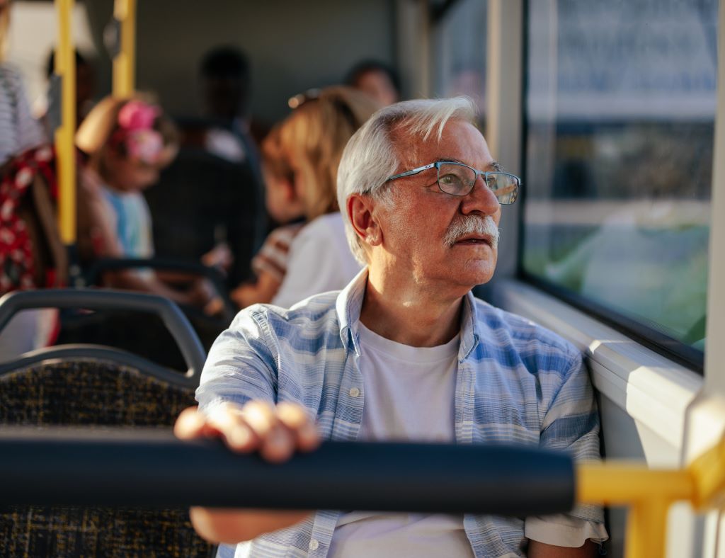 Older adult man looks out the window as he rides the bus