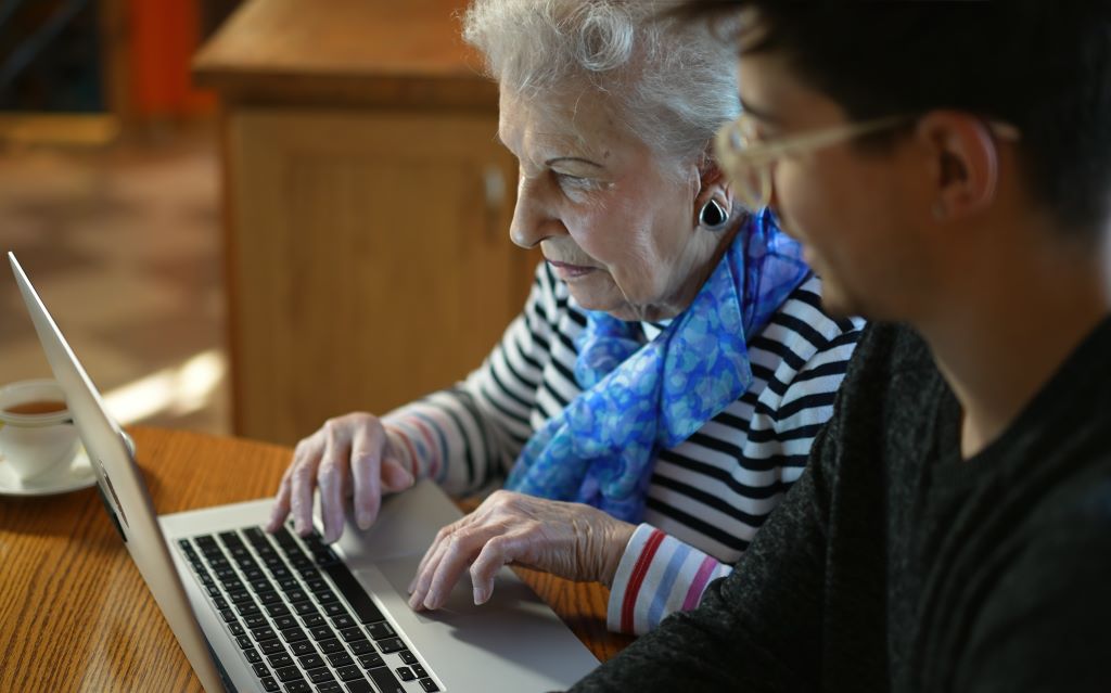 Older adult woman looks at Medicaid help on her computer with a caregiver