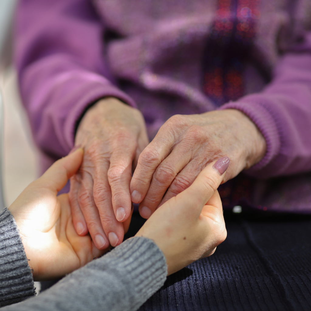 Up close image of two people holding hands. One is elderly, one is younger.