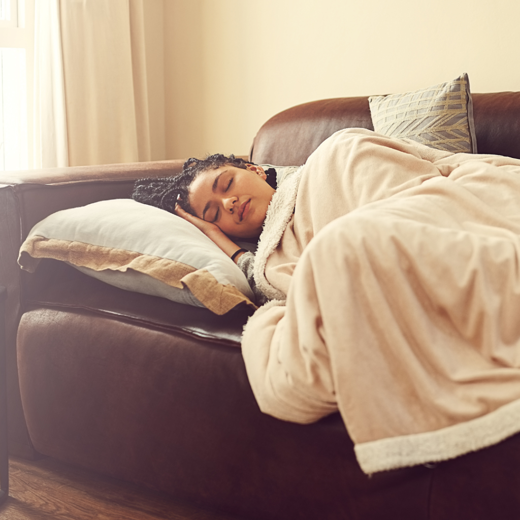 a woman taking a nap on a couch with a blanket covering her.