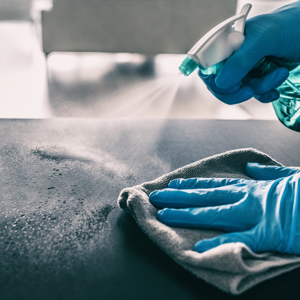 Up close shot of gloved hands spraying a bottle of cleaner onto a countertop and wiping with a towel