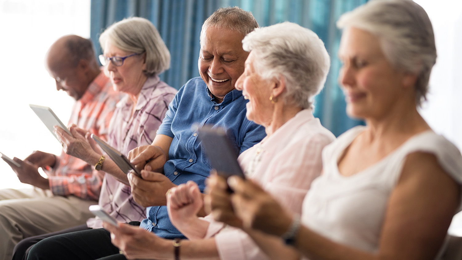 Older adults laugh and smile as they use tablets together