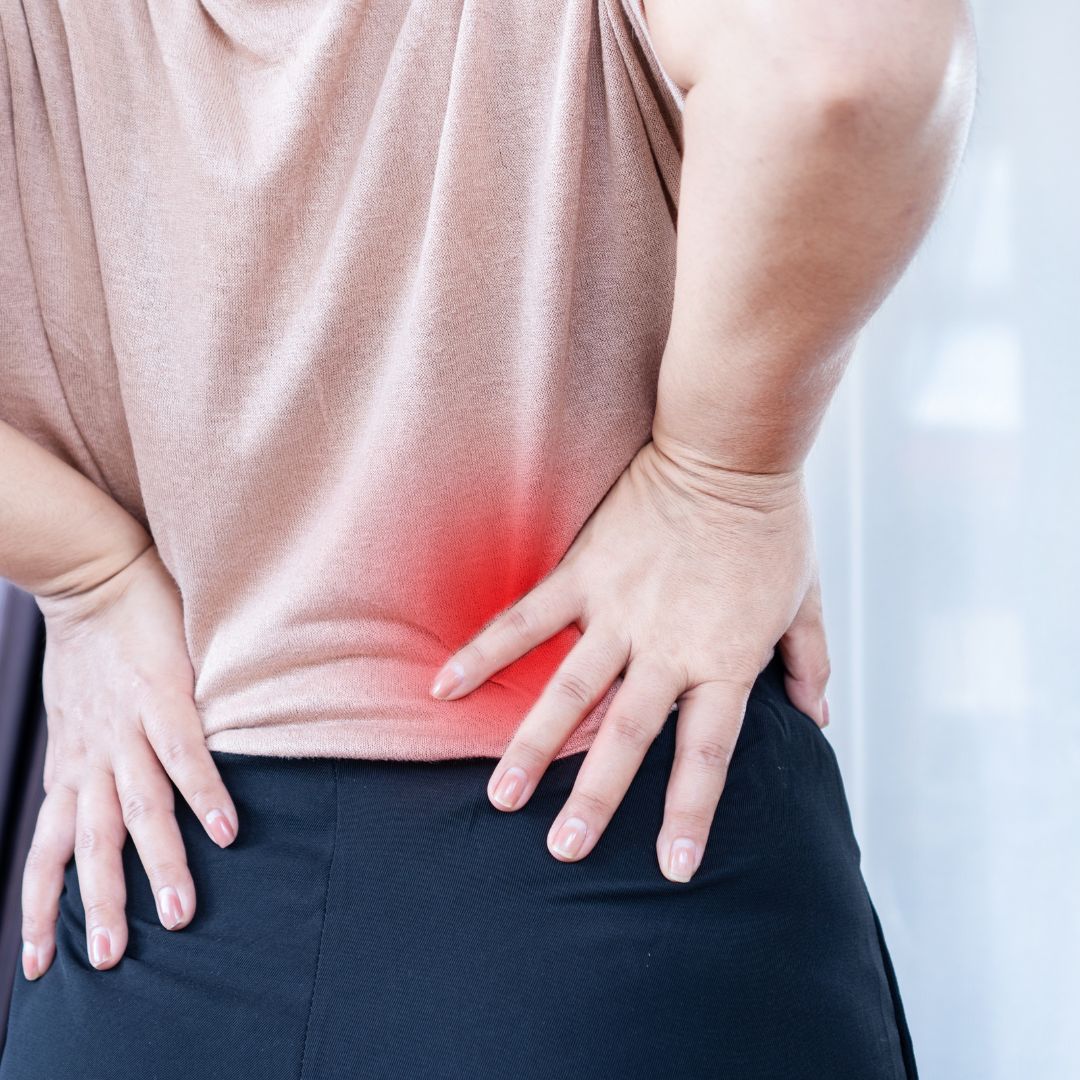 Person holding their lower back in pain, with a red highlighted area indicating discomfort or strain