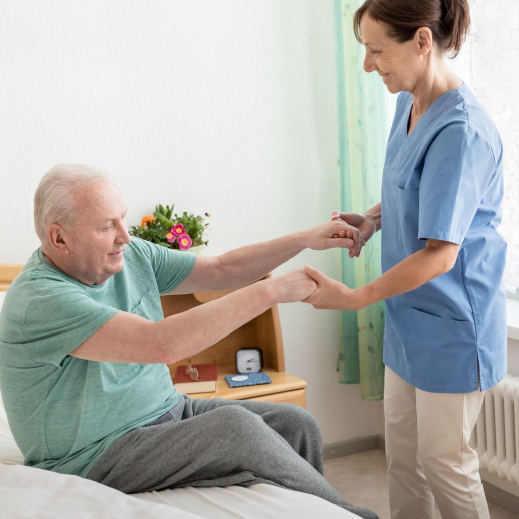 A woman helping an elderly man get up out of the bed