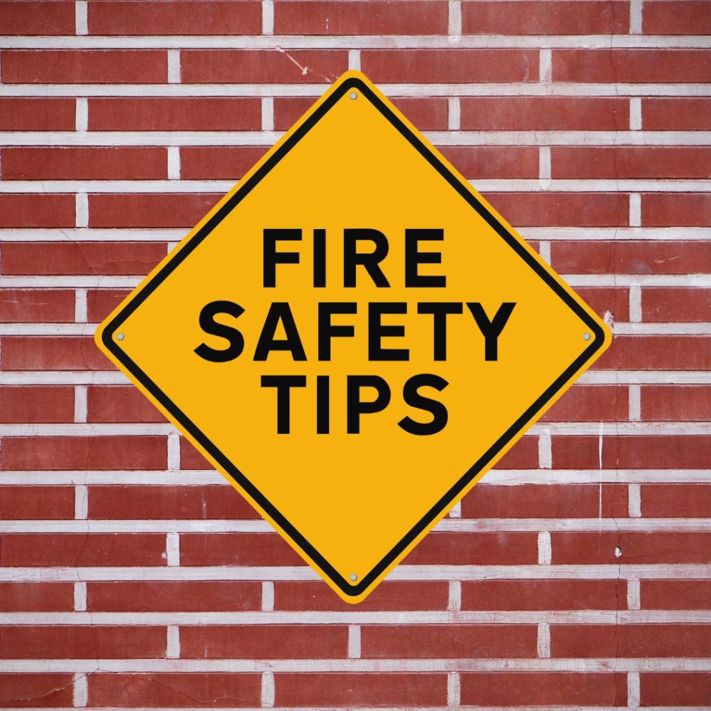  Yellow diamond-shaped sign with the text "Fire Safety Tips" against a red brick background.