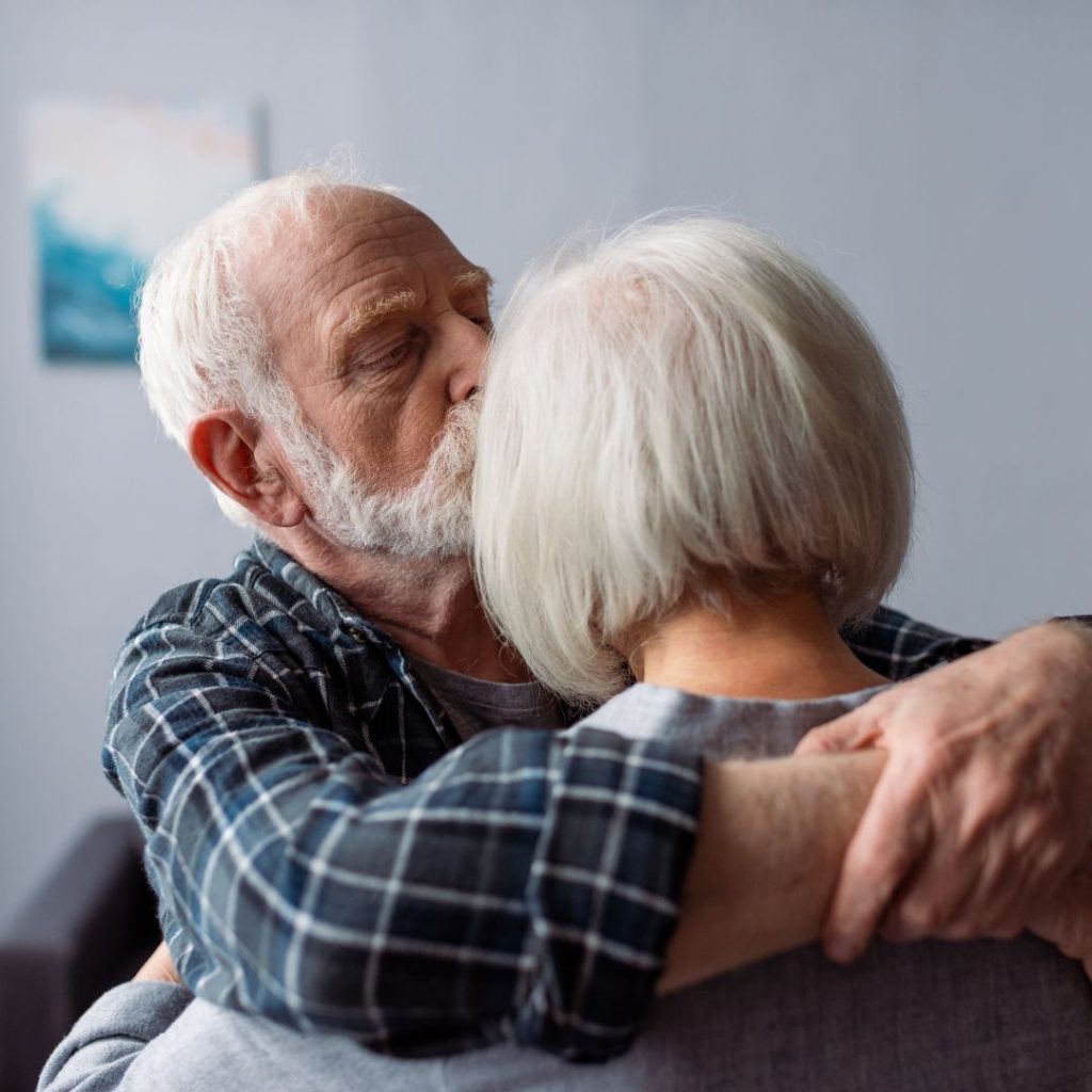 Elderly man gently kissing the head of a woman during an emotional embrace.
