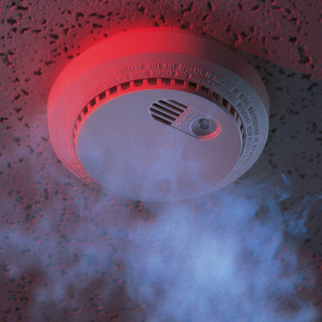 Smoke detector with visible smoke and red light on ceiling.