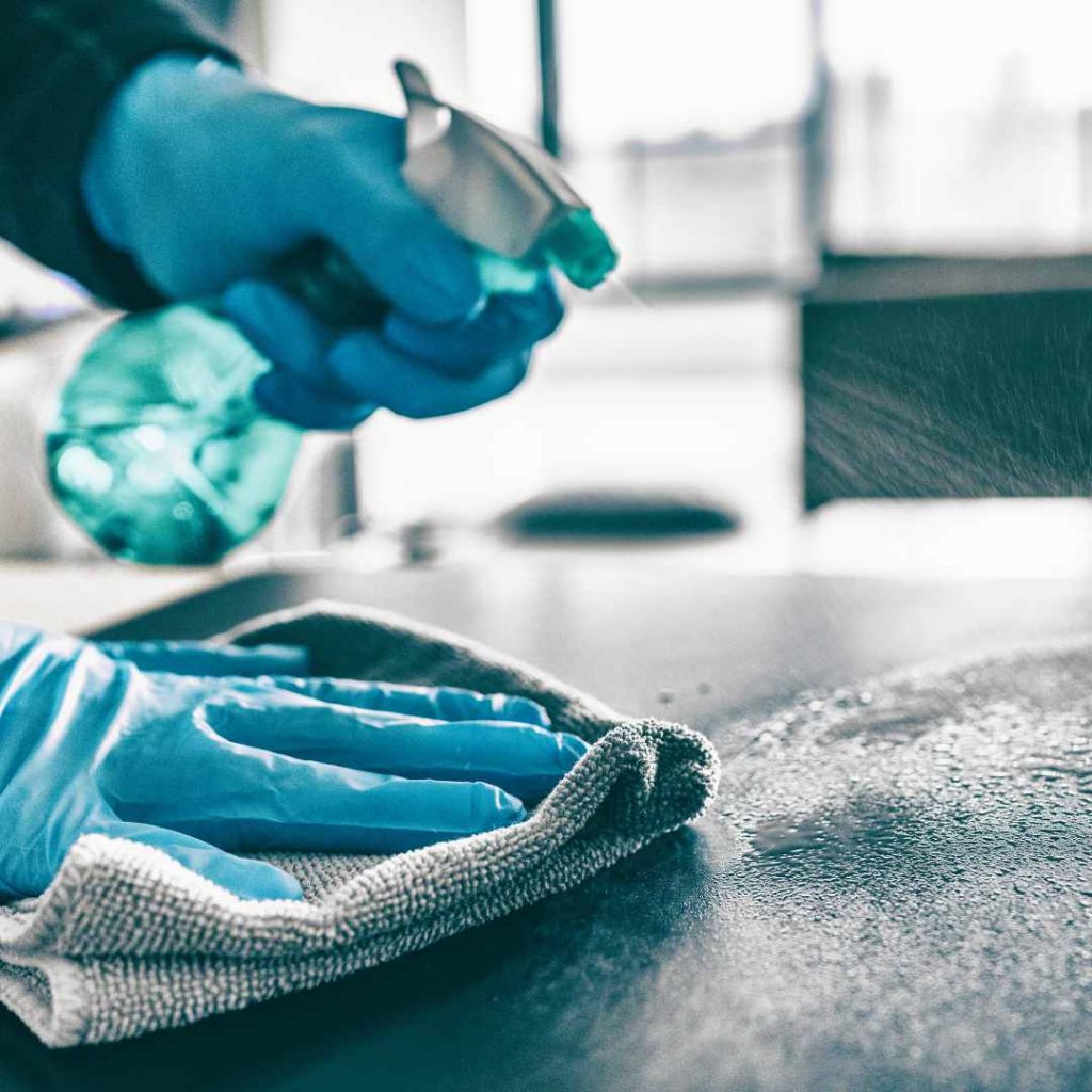 Person cleaning a surface with spray bottle and cloth while wearing gloves