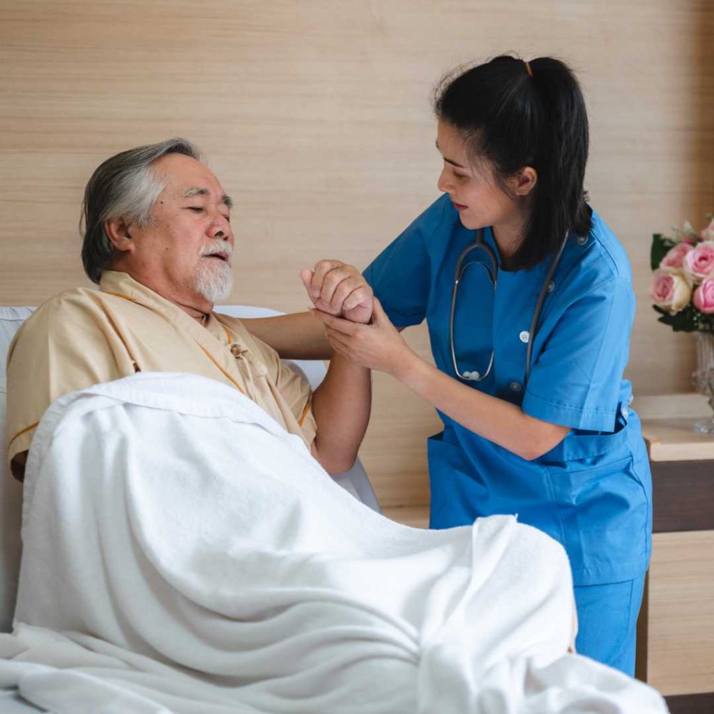 Female nurse assisting an elderly male patient in a hospital bed.
