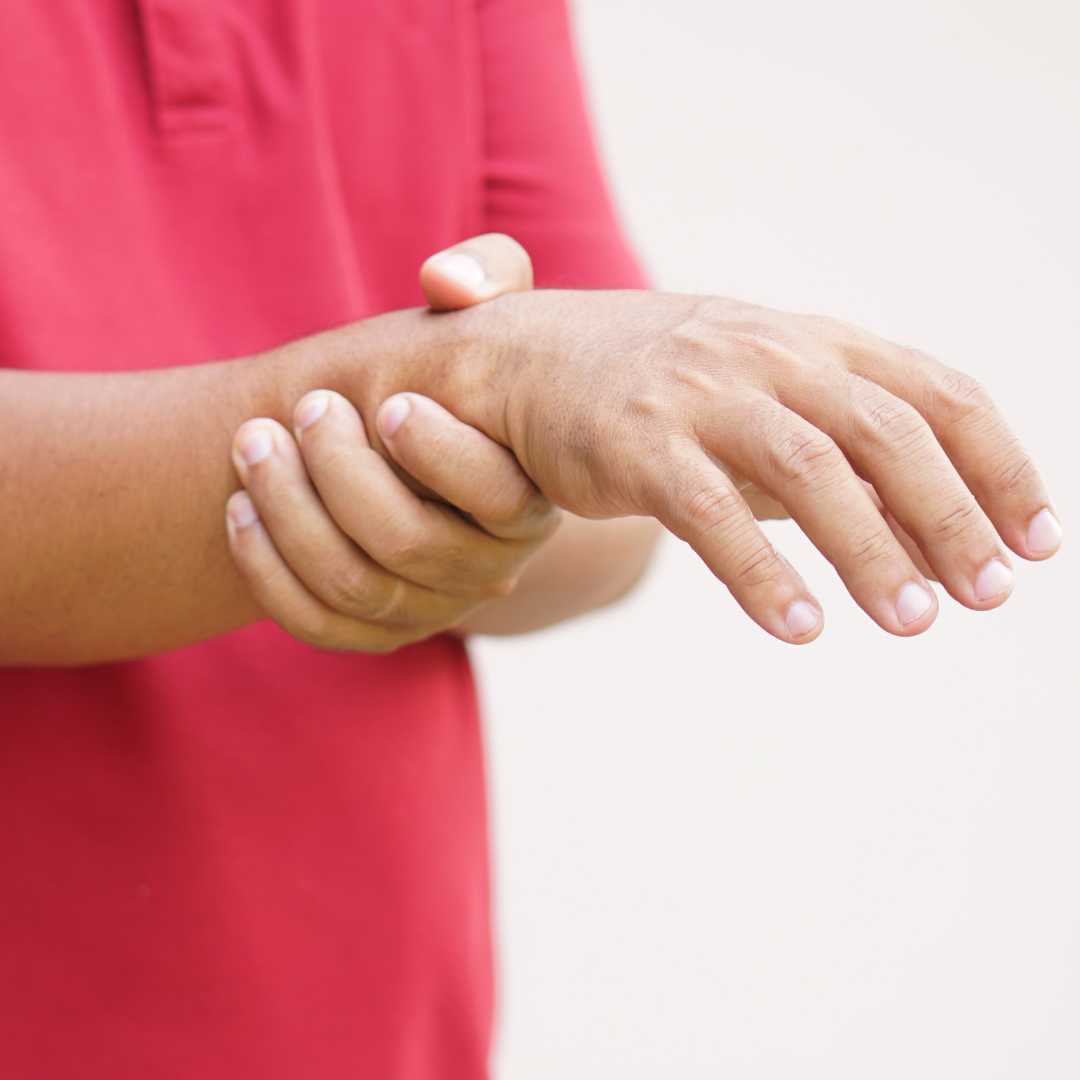 Person in a red shirt holding their wrist, appearing to experience arm pain.