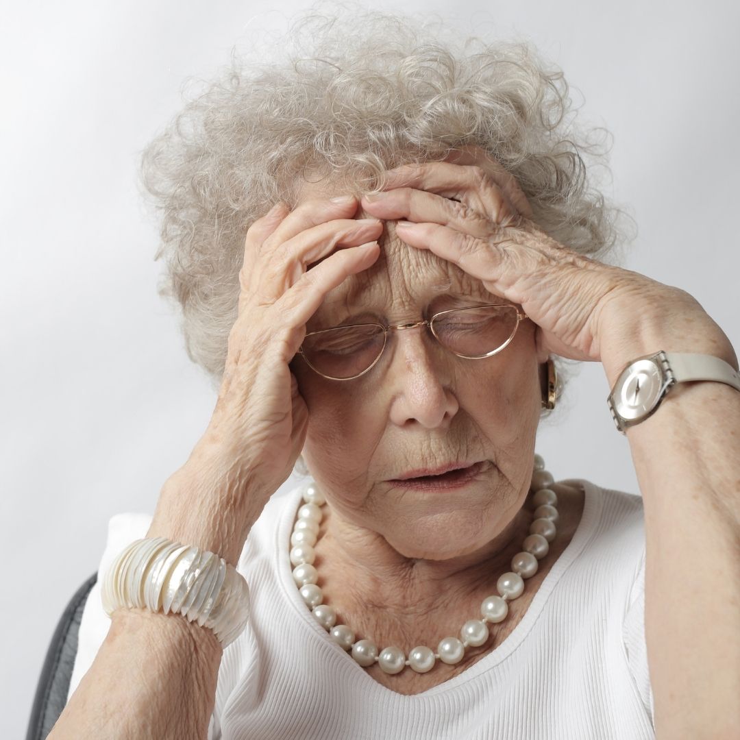 An elderly woman holds her head with a pained expression.