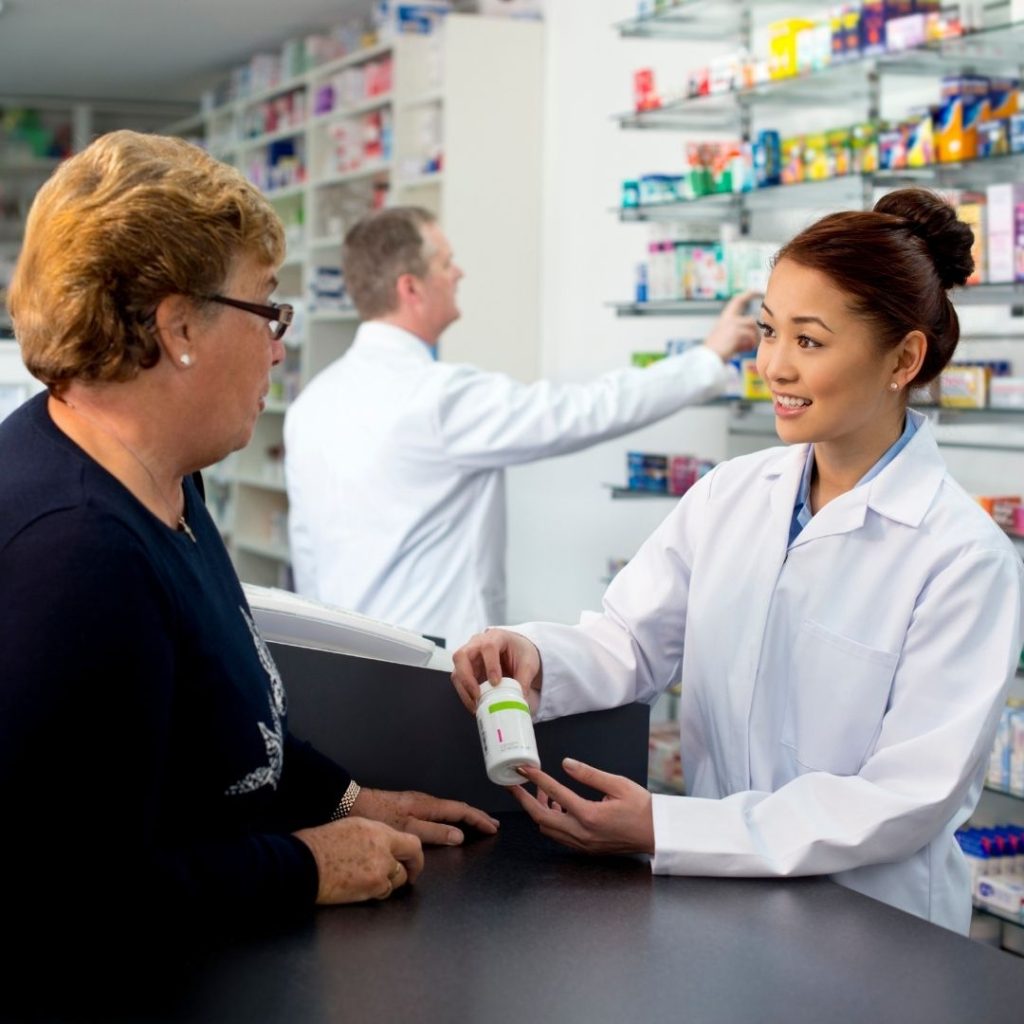 Pharmacist smiles while explaining a prescription bottle to an older customer.