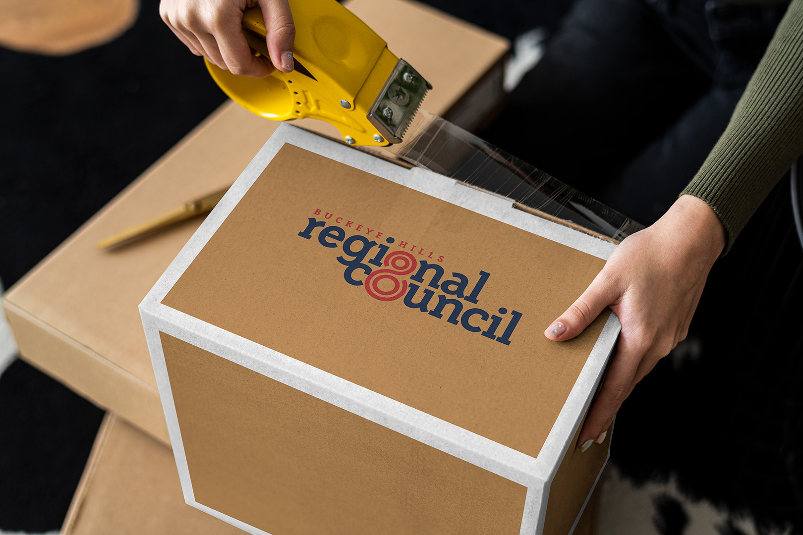 A person's hands sealing a moving box with packing tape.