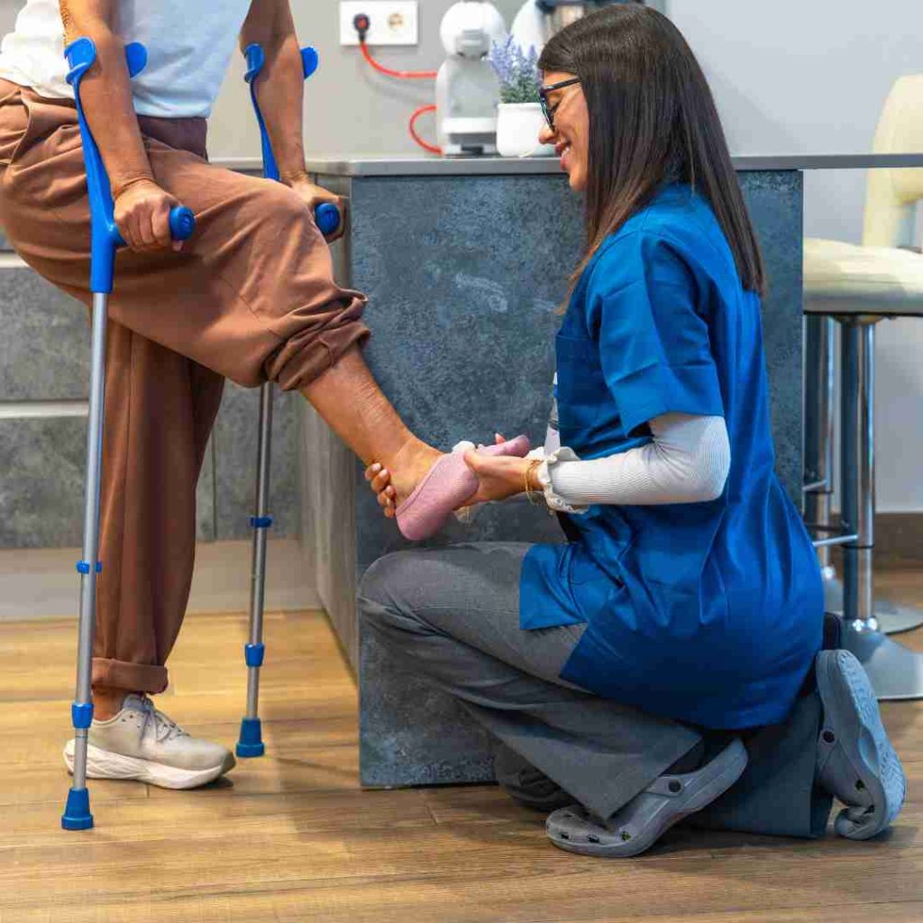 Clinician kneels to support foot of person using crutches.