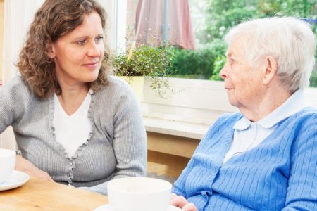 A caregiver and an older adult have a conversation over coffee.