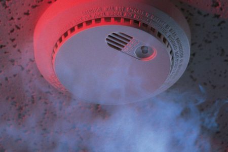 Smoke detector with visible smoke and red light on ceiling.