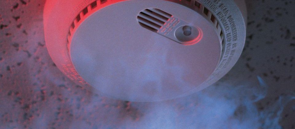 Smoke detector with visible smoke and red light on ceiling.