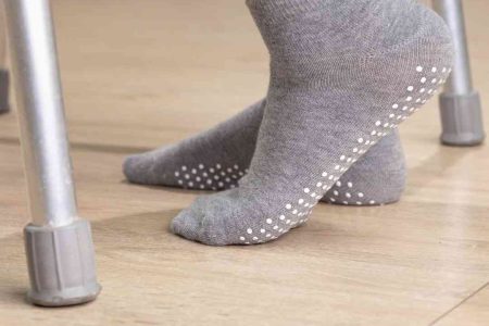 Up close view of gray grip socks on a hardwood floor. Walker is visible indicating an older adult with mobility issues.