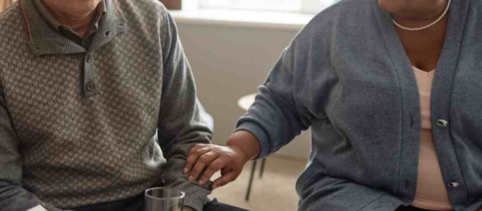 Two individuals in a support group setting. One is an older white male, the other is a middle-aged African American woman.