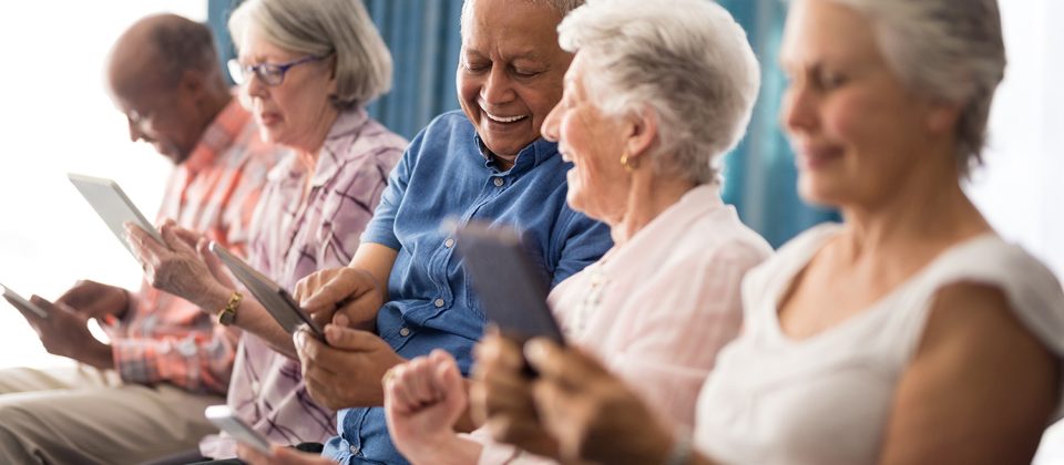 Older adults laugh and smile as they use tablets together