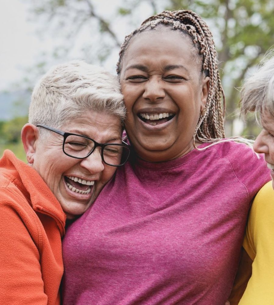 Three older adult woman hug and laugh together