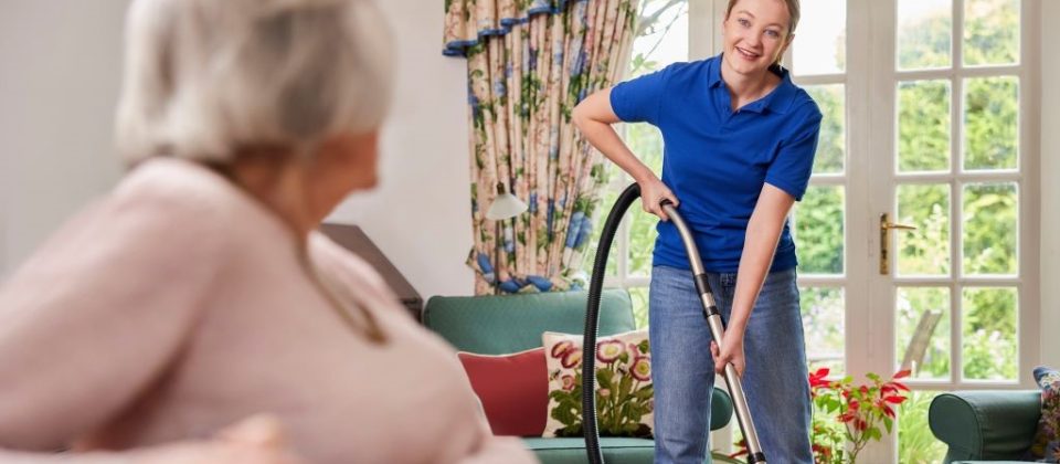 Older adult woman watches her caregiver clean the house