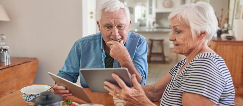 Older adult couple looking at Medicaid versus Medicare on tablets.