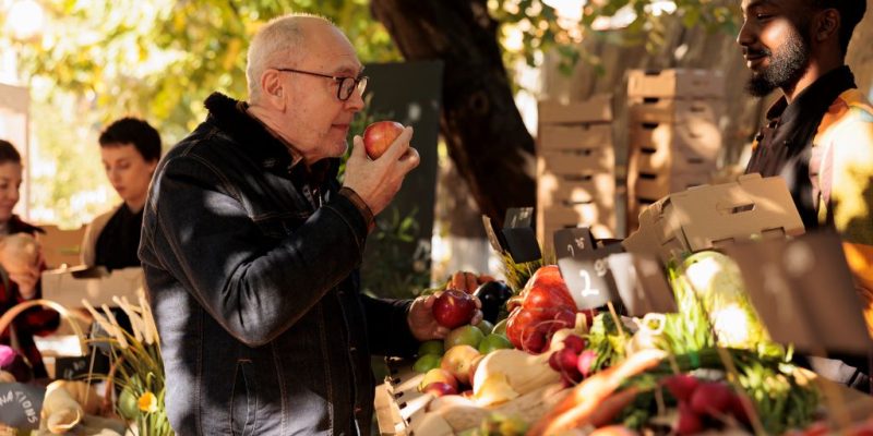 Older adult man smells an apple at a farmers market