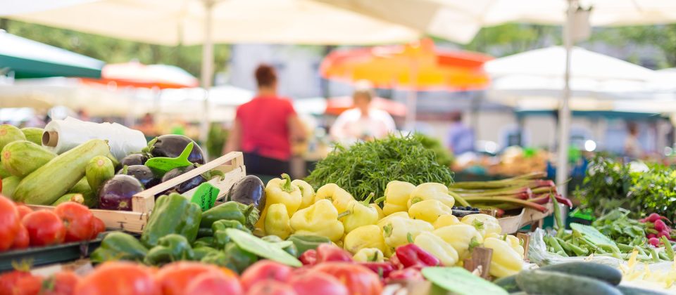 An variety of vegetables at a farmers market stand, including tomatoes, peppers, squash, eggplant, and beans