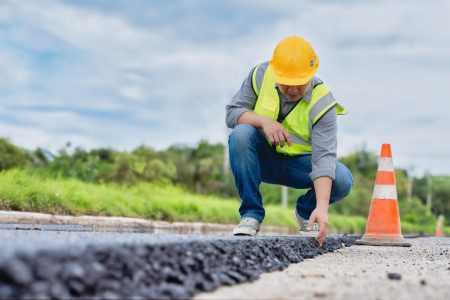 A worker inspects new asphalt on a road.