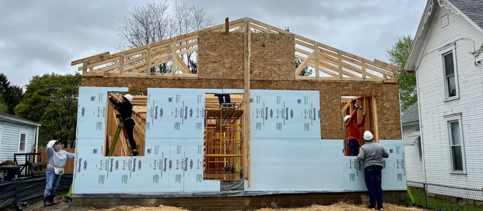 Volunteers and tradespeople work on a Habitat for Humanity home construction site.