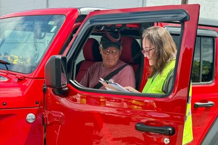 A CarFit volunteer with checklist in hand speaks with a driver.