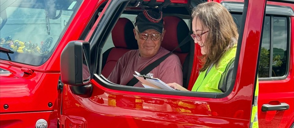 A CarFit volunteer with checklist in hand speaks with a driver.